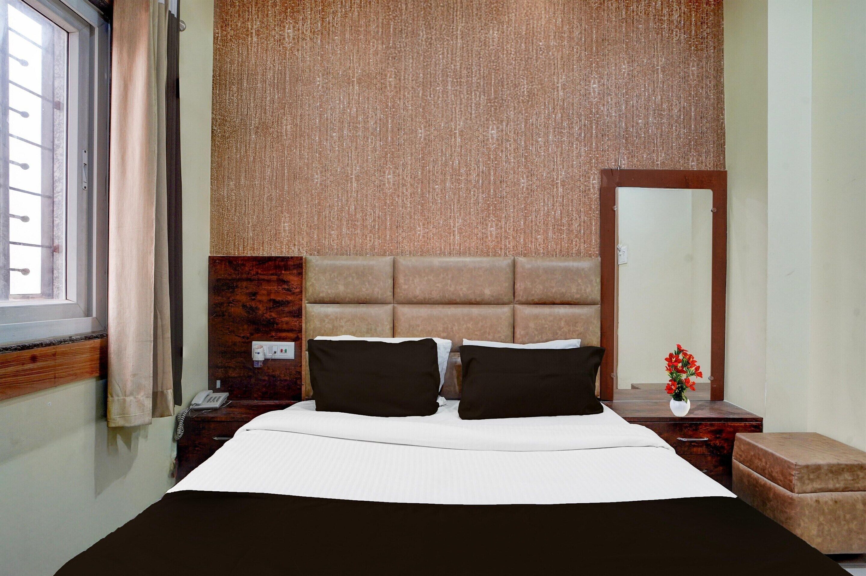 Habitación de hotel con cama, mesita de noche, teléfono, espejo y ventana con cortinas.