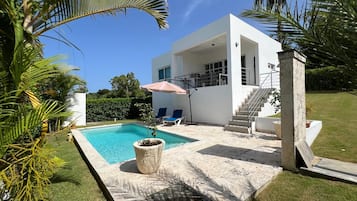 Et moderne hus med swimmingpool, udendørs møbler og en trappe op til en balkon.