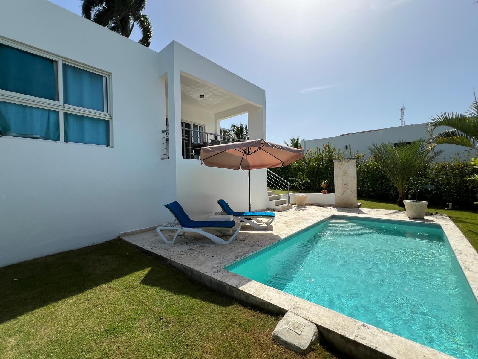 A modern house with a swimming pool, two blue lounge chairs, and a large umbrella.
