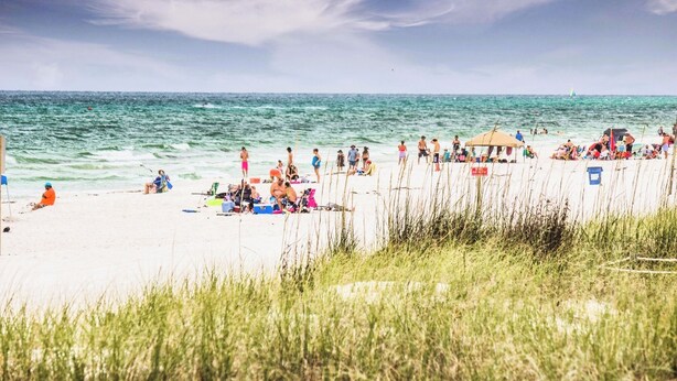A beach with people sunbathing and swimming, a beach umbrella, and a lifeguard tower. - Mins Walk to Laguna Beach! King Suite, BBQ, Pool, Private Patio & Free parking (Panama City Beach)