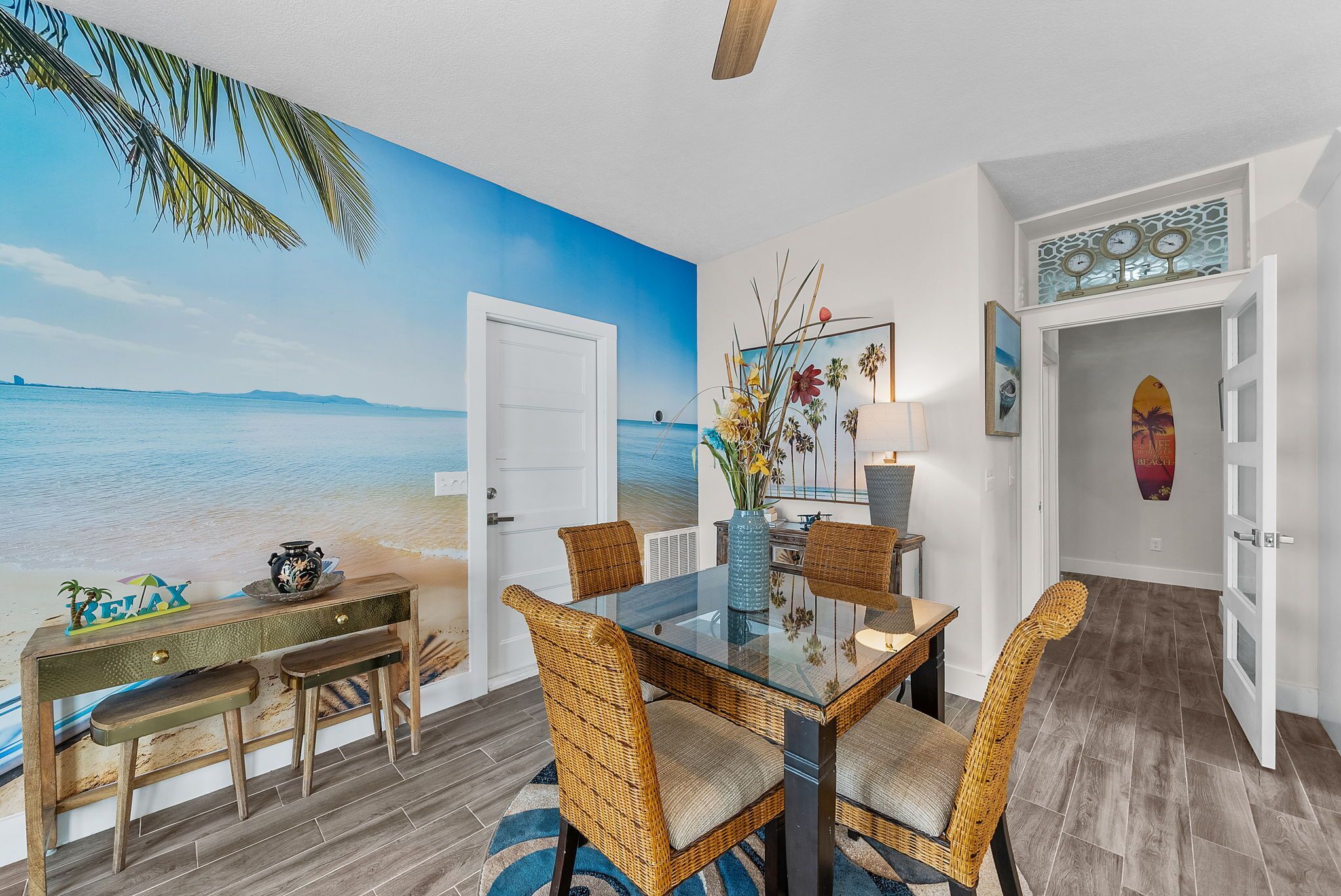 A dining area with a glass table, wicker chairs, and a view of the ocean through a mural.