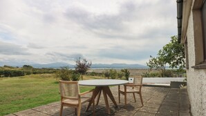 Un patio al aire libre con dos sillas de madera y una mesa, con vistas a una zona verde y montañas distantes.