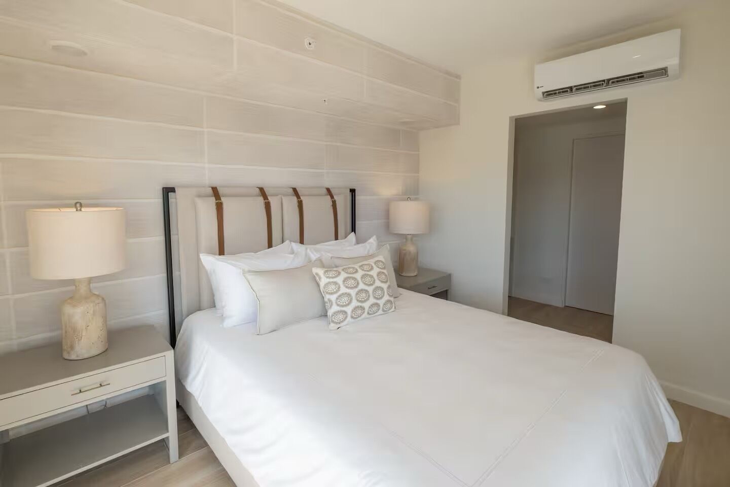 Une chambre à coucher comprenant un lit, deux tables de chevet, une commode, un climatiseur fixé au mur et une porte.