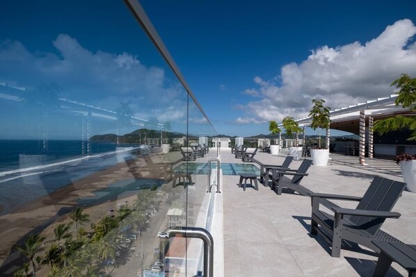 A rooftop pool area with lounge chairs, a pool, and a view of the beach and ocean. - Pacific Point 1106A (Jaco)