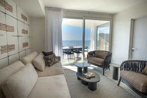 A modern living room with a sofa, two armchairs, a coffee table, and a balcony with a view of the sea. - Pacific Point 1106A (Jaco)