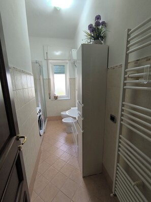 Un baño con ducha, inodoro, lavabo, una ventana con persianas y un perchero para toallas.