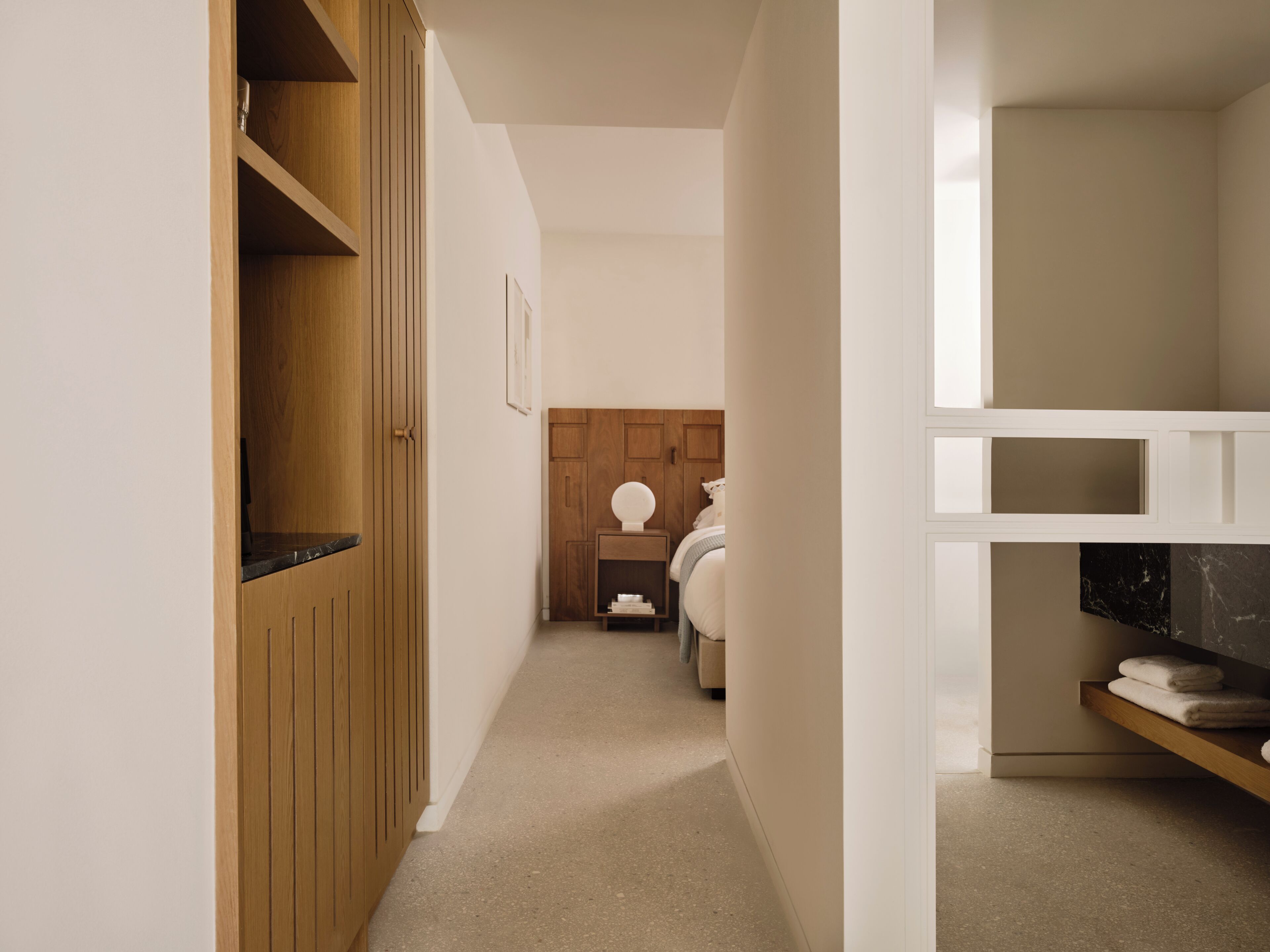 A narrow hallway with wooden cabinets, a bed with a headboard, and a white wall.