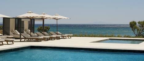 Una piscina con sillones de descanso y sombrillas, vista despejada al mar y una zona de piscina pequeña.