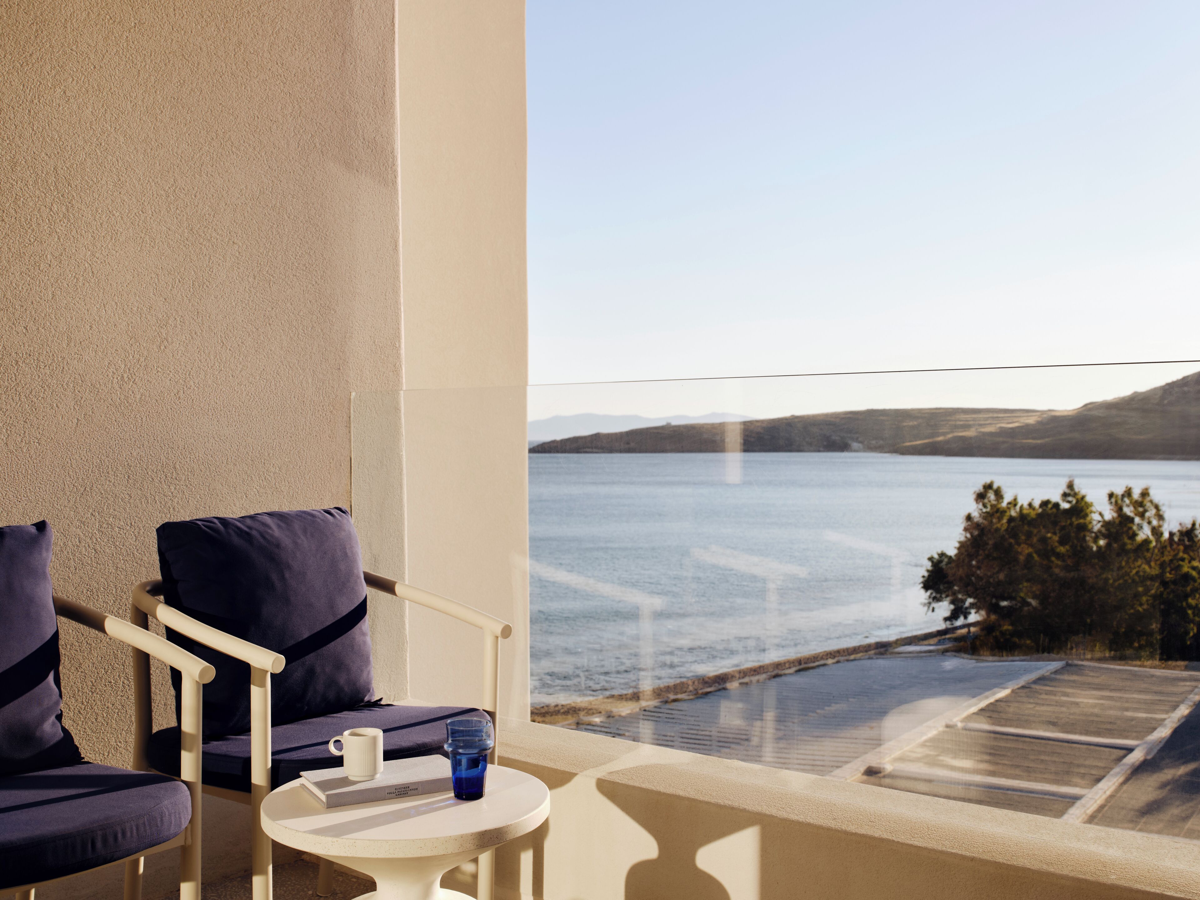 Ein Balkon mit zwei Stühlen, einem kleinen Tisch und Blick auf ein Gewässer.