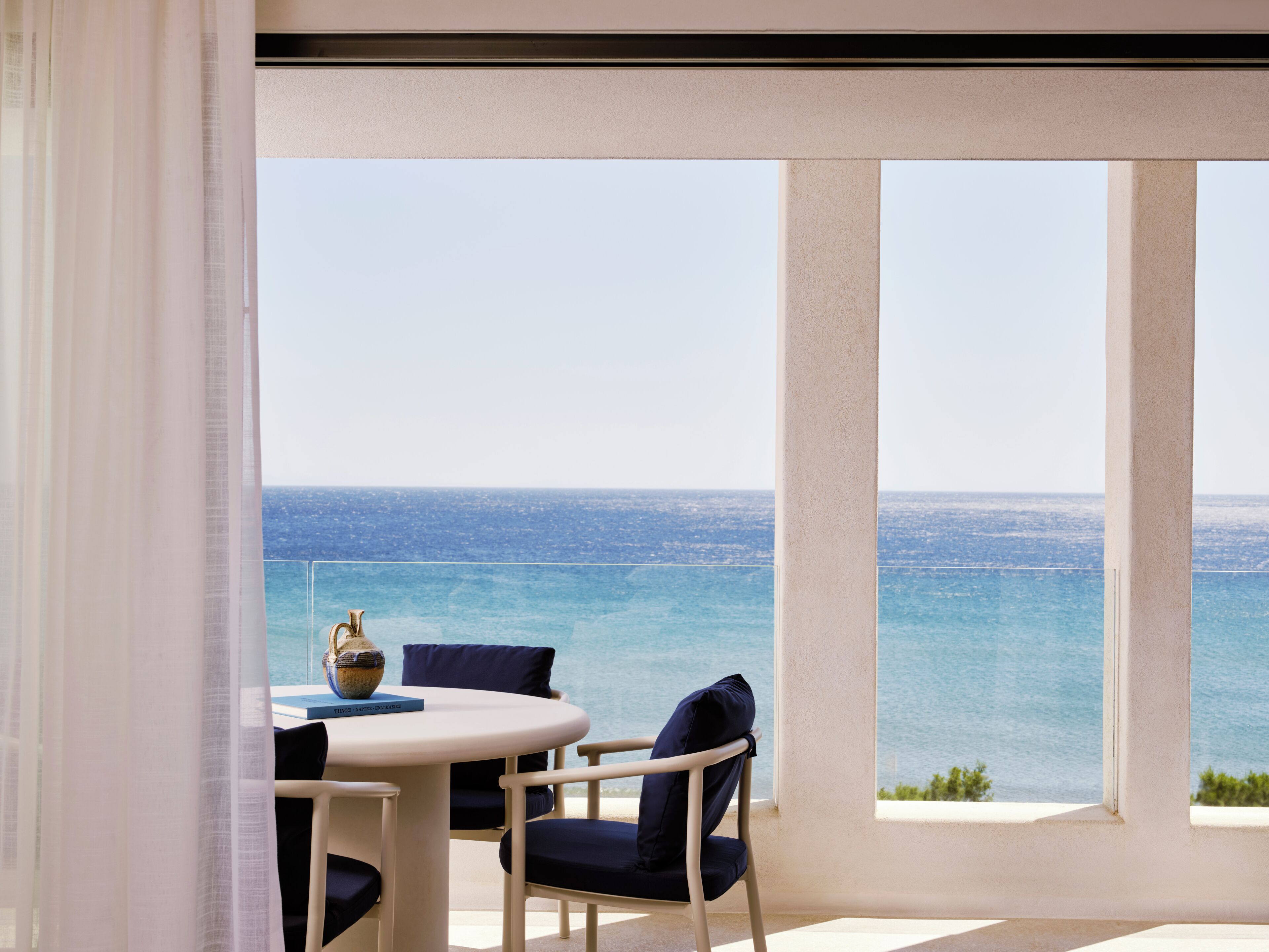 A balcony with a table and chairs, overlooking a body of water.