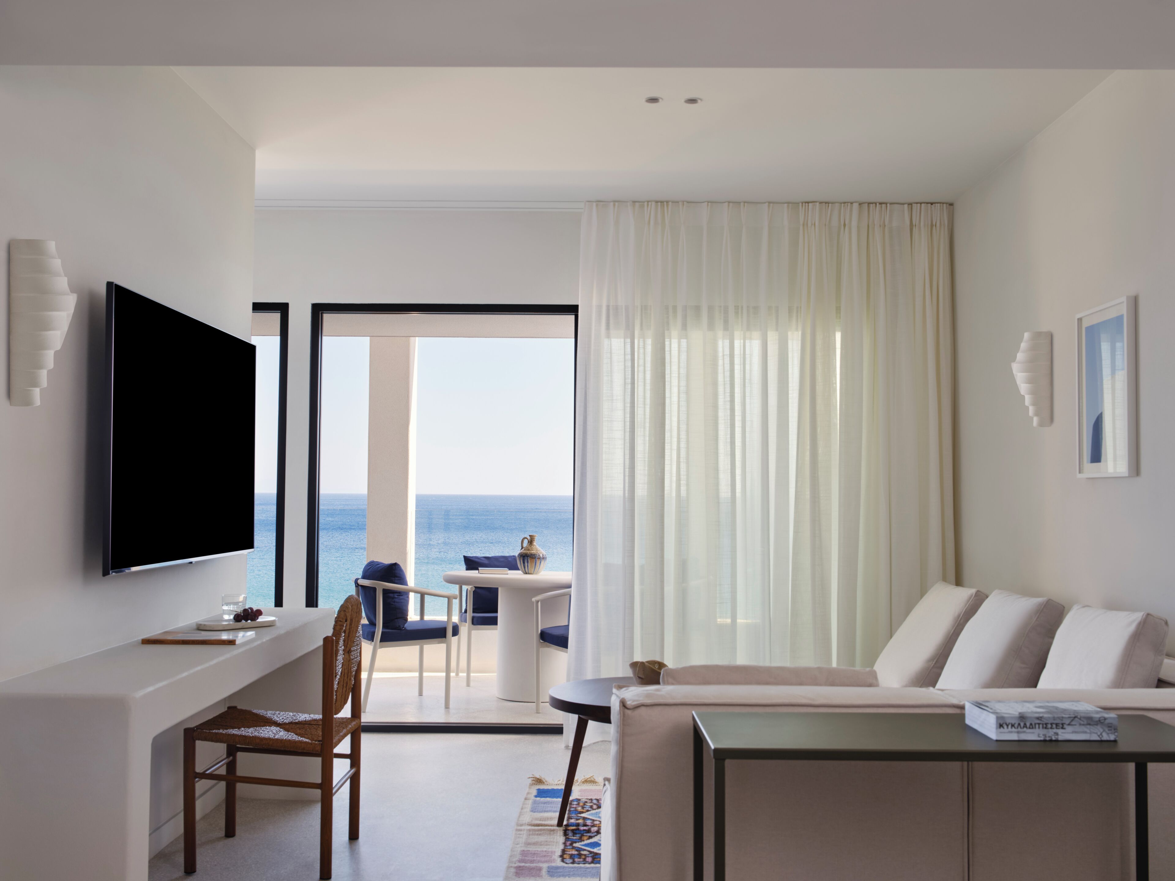 Habitación de hotel con televisor de pantalla plana, sofá, mesa de comedor y vistas al mar.
