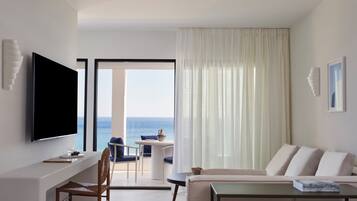 Habitación de hotel con televisor de pantalla plana, sofá, mesa de comedor y vistas al mar.
