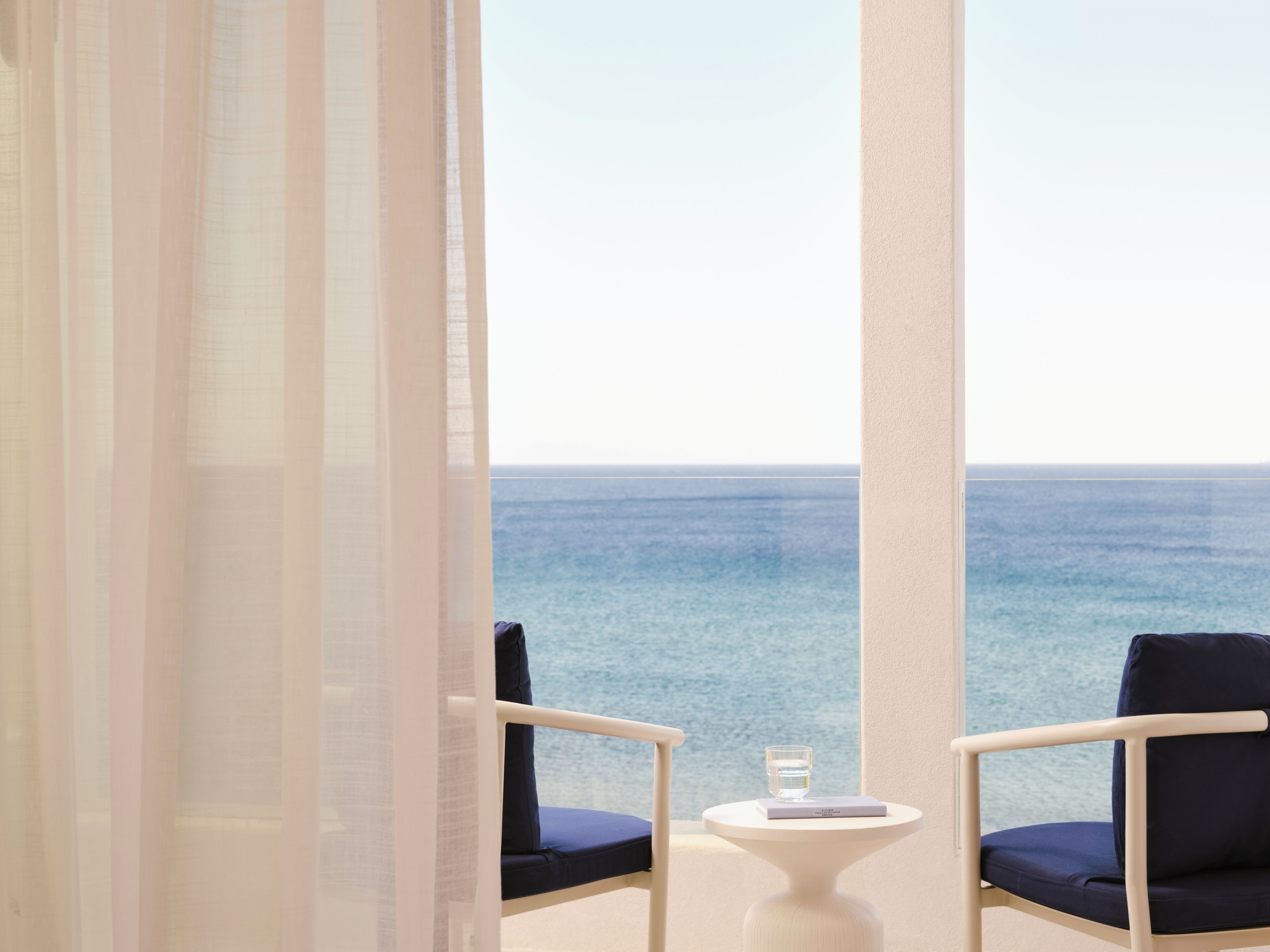 A balcony with two chairs, a small table, and a glass of water.