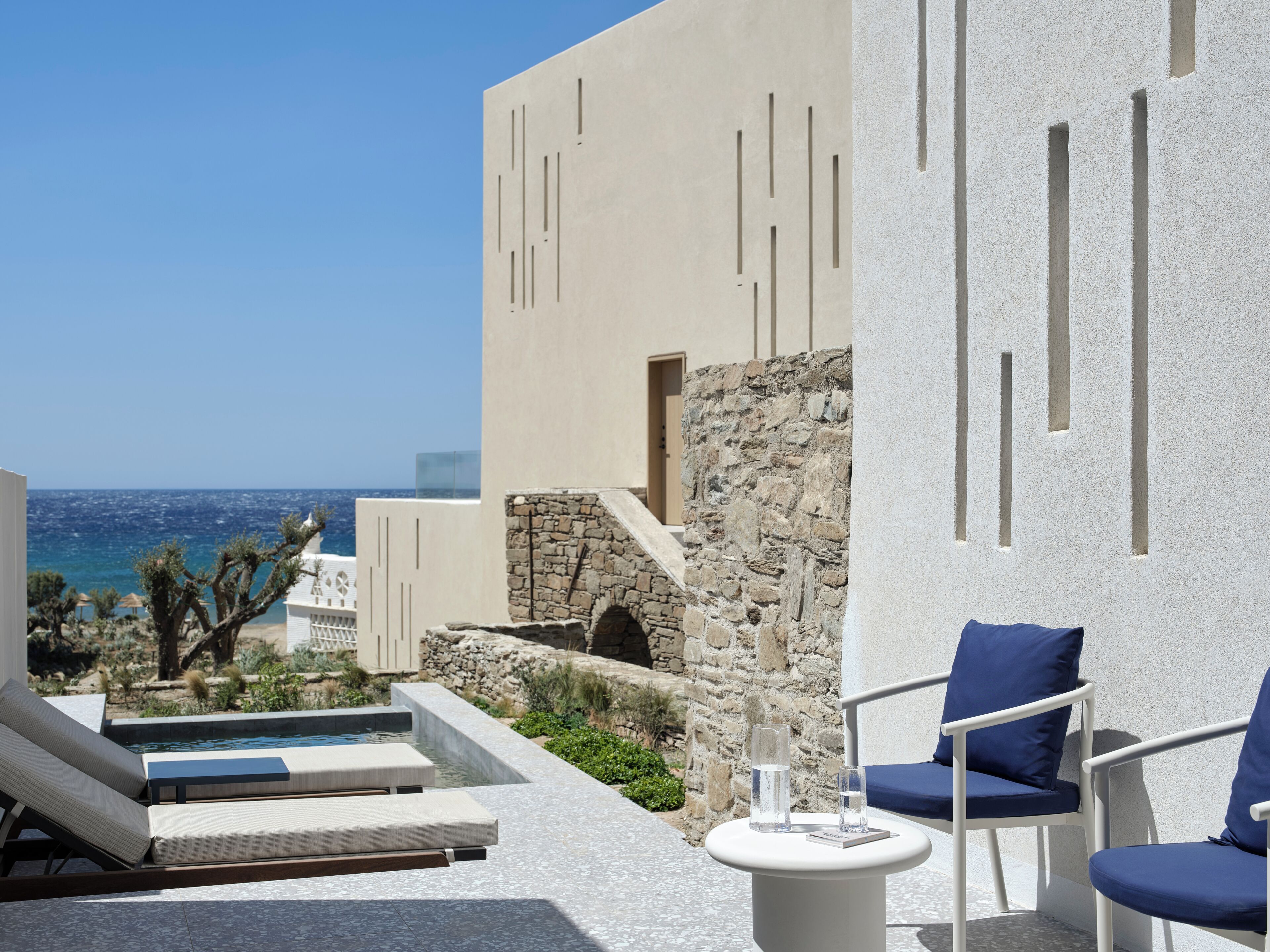 A poolside area with lounge chairs, a small table, and a view of the sea.