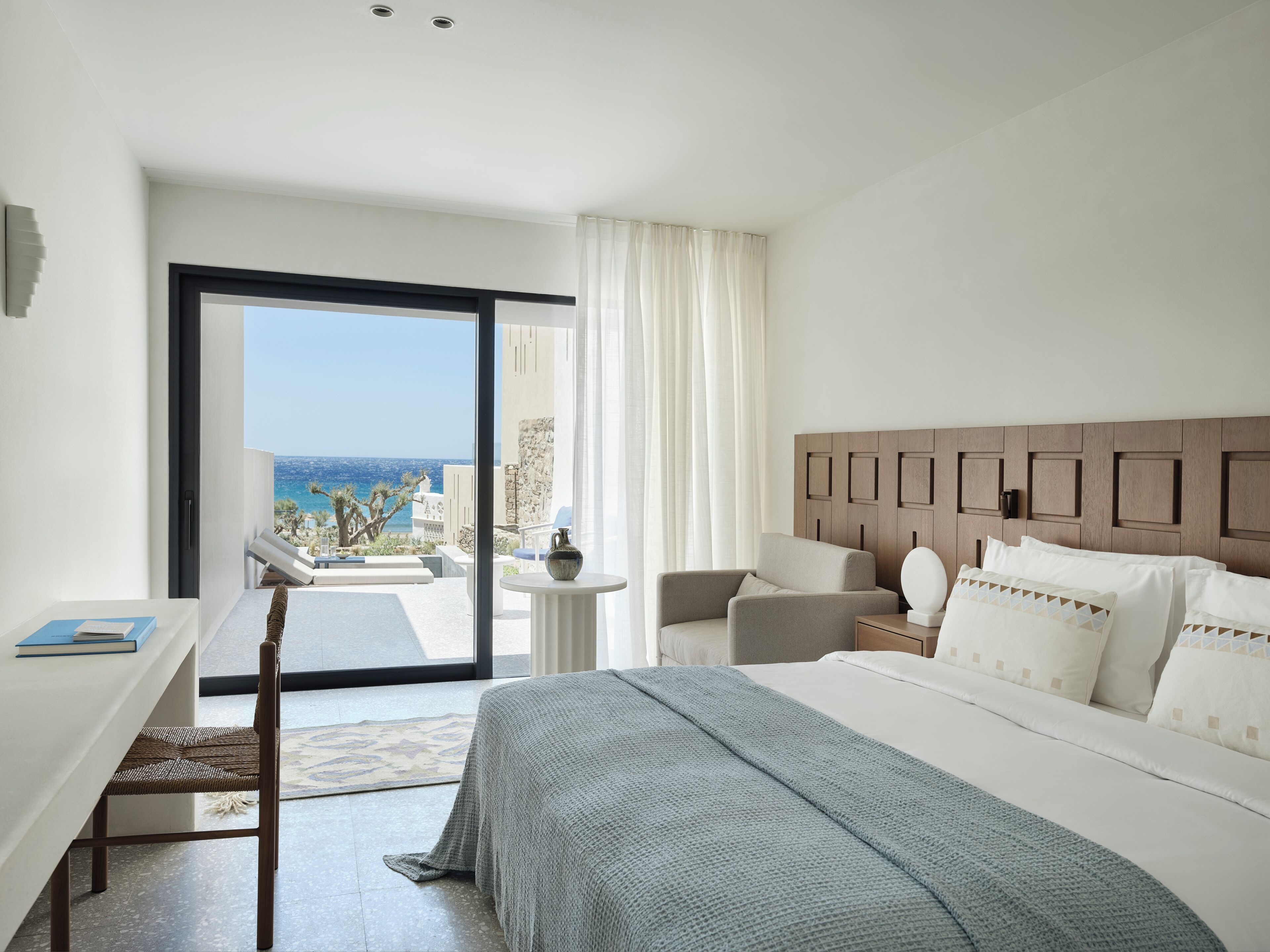 A hotel room with a bed, a desk, a chair, a view of the sea, and a balcony.