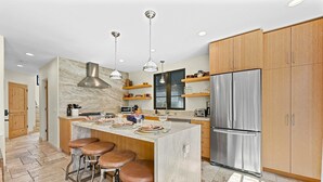 A modern kitchen with a central island, stainless steel appliances, wooden cabinets, and pendant lighting. - Casa al Mare - Boho Mission Beach Retreat w/ A/C (San Diego)