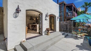 A building with a white exterior, a wooden deck with outdoor seating, and a large umbrella. - Casa al Mare - Boho Mission Beach Retreat w/ A/C (San Diego)
