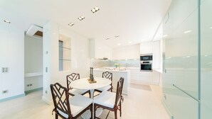 Una cocina moderna con armarios blancos, una isla central y un comedor con una mesa redonda y sillas.