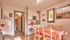 A compact living space with a kitchenette, a dining area with a table and chairs, a sofa, and a washing machine.