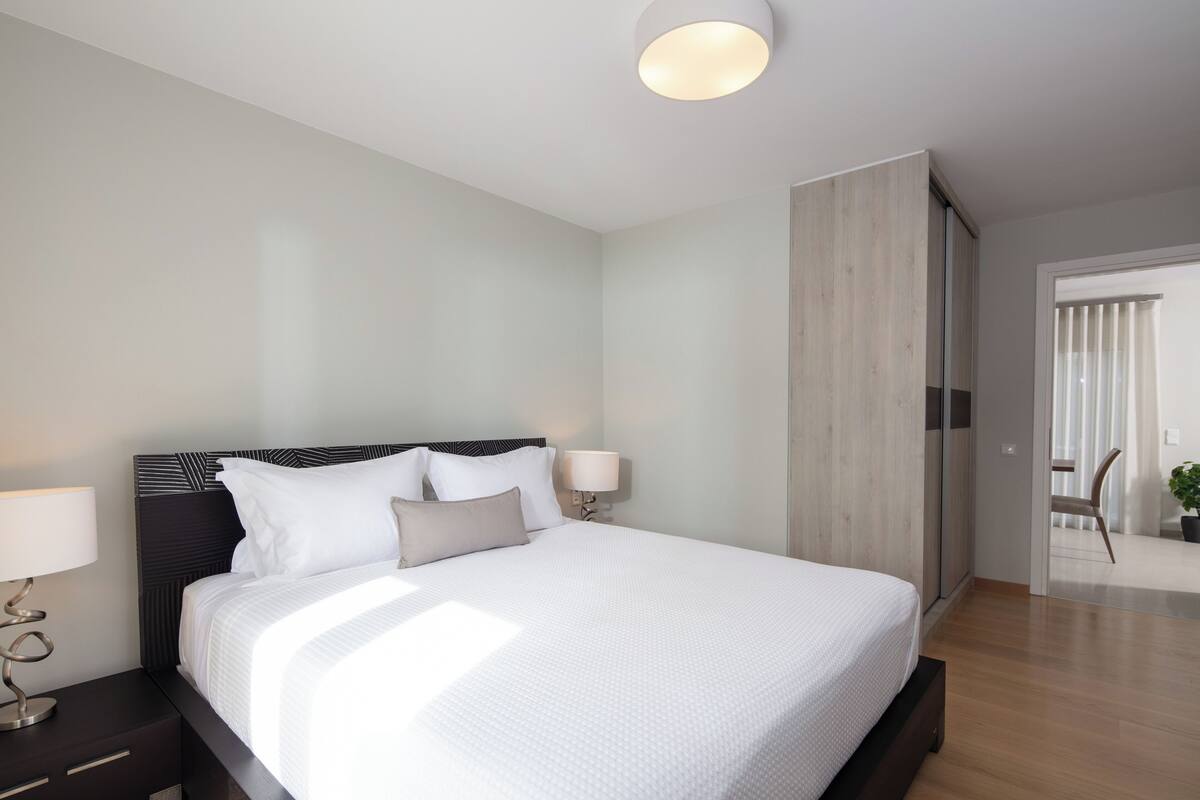 Une chambre d’hôtel moderne dotée d’un grand lit, d’une table de chevet, d’une lampe fixée au mur et d’une porte coulissante donnant accès à la salle de bain.