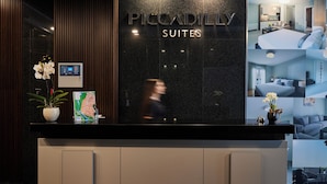 Un mostrador de recepción de hotel con un cartel de Piccadilly Suites, una pantalla digital y una orquídea en maceta.