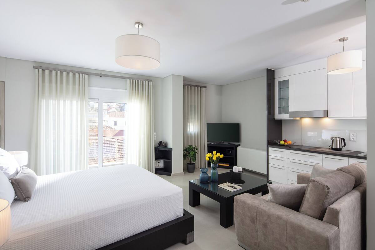 Une chambre d’hôtel moderne équipée d’un lit, d’un bureau, d’un canapé, d’une télévision et d’une kitchenette.
