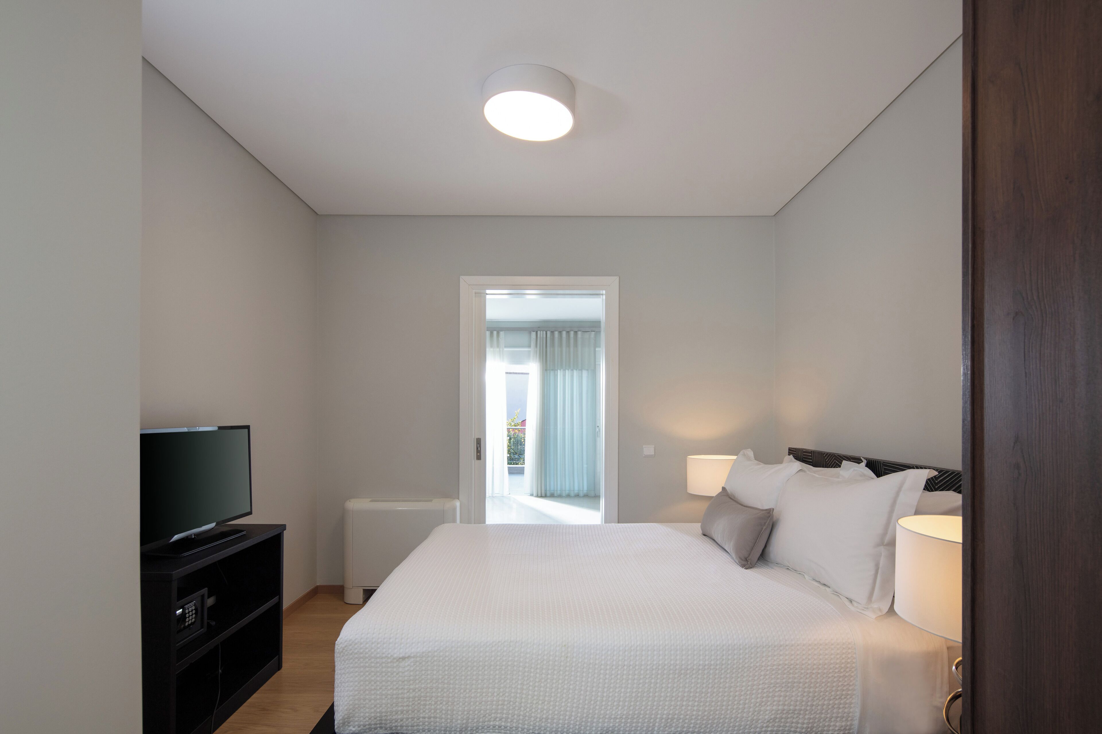 Ein Schlafzimmer mit einem Bett, einem Fernseher und einer Tür, die auf einen Balkon führt.