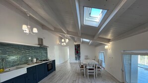 Una cocina amplia con una isla central, un comedor con mesa y sillas, y un tragaluz grande.