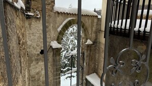 Una escalera exterior cubierta de nieve con barandilla de metal, que lleva a un edificio de piedra con una entrada arqueada.