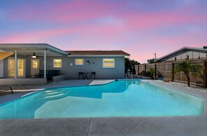 Un jardin avec une piscine, une terrasse couverte et une clôture en bois.