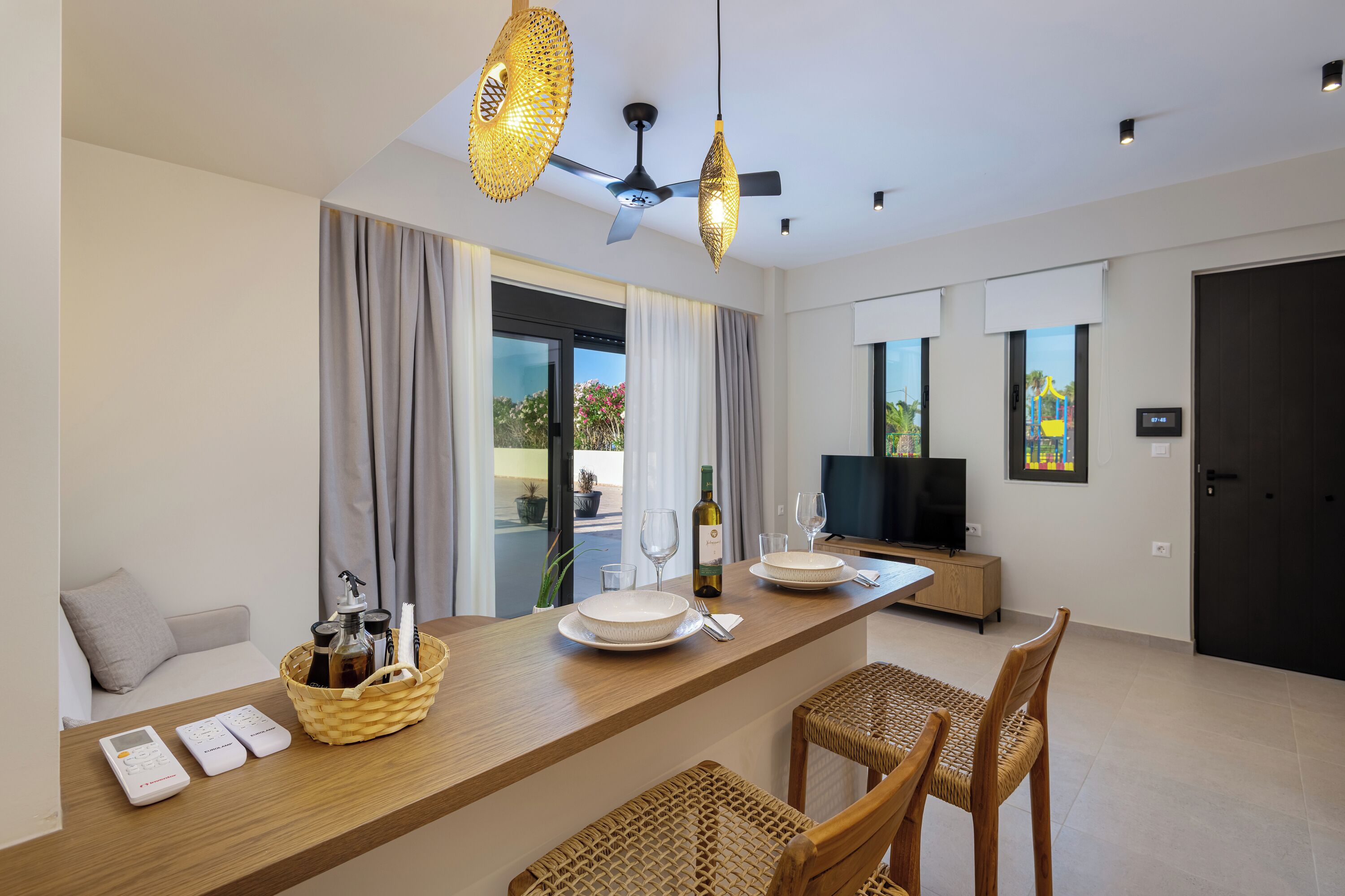 A modern hotel room with a dining area, a television, and a large window with curtains.