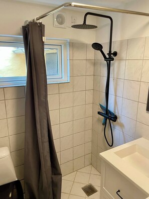 A shower with a handheld showerhead, a window, and a white sink.