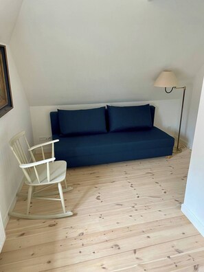 A room with a blue sofa, a rocking chair, a floor lamp, and a wooden floor.