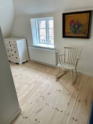 A room with a radiator, a window, a white dresser, and a rocking chair.