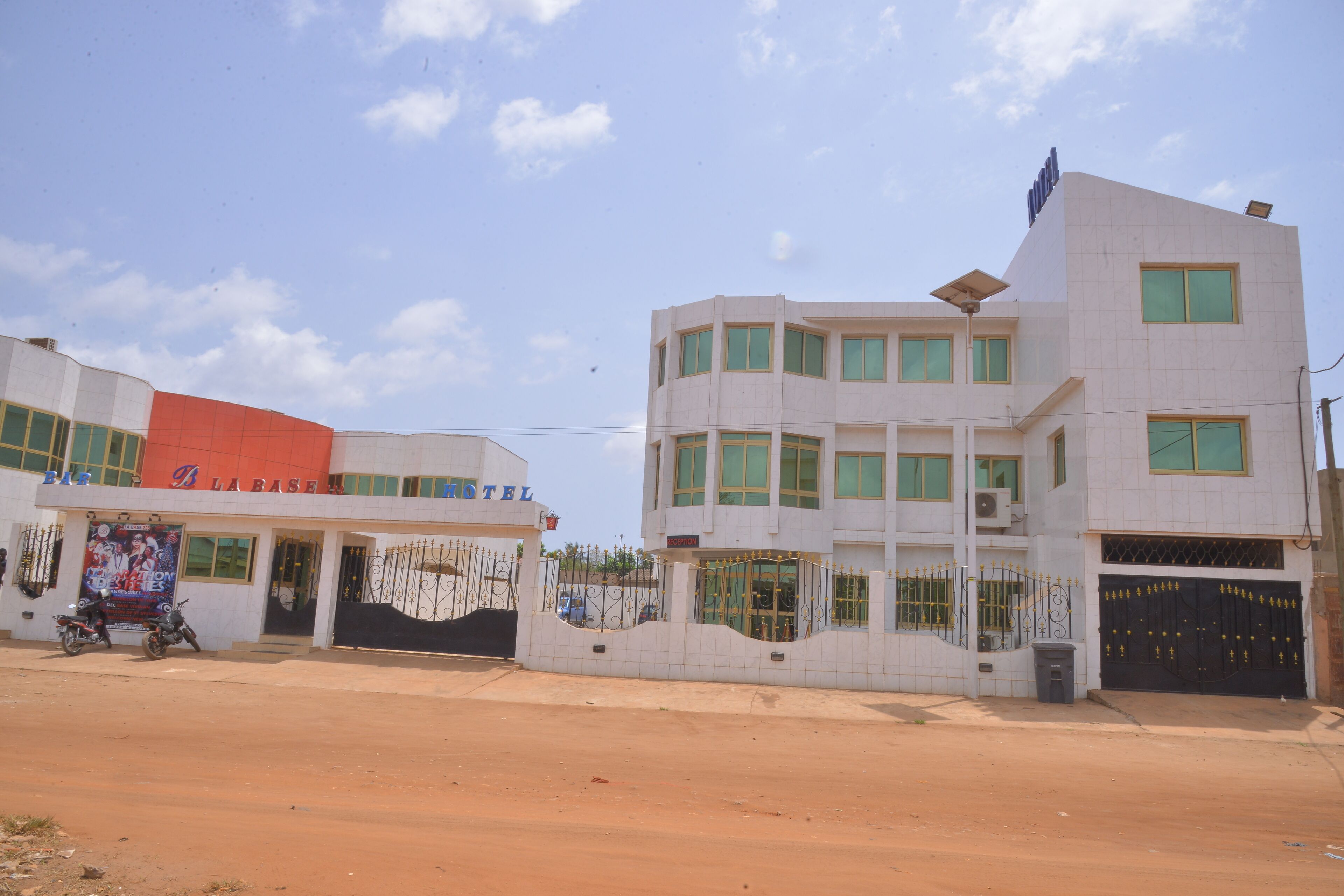 A hotel with a white exterior and a red roof. It has multiple windows and a gated entrance.