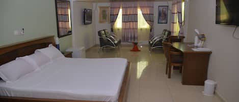 Une chambre d’hôtel avec un lit, un bureau, deux chaises, une télévision et une fenêtre avec des rideaux.