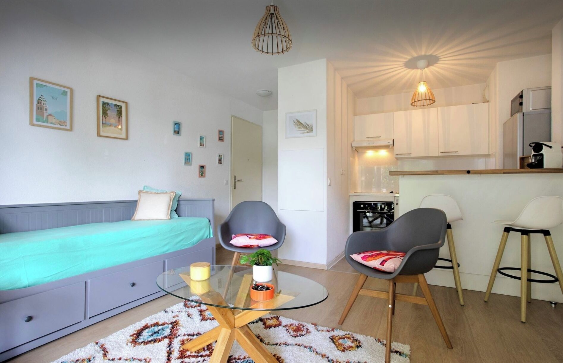 Un appartement moderne comprenant un canapé, deux fauteuils, une table en verre, un coin cuisine et une table à manger.