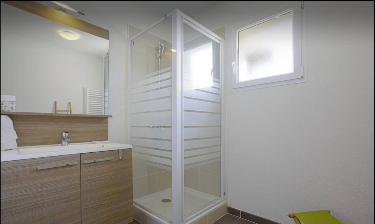 Un bany amb plat de dutxa, un lavabo amb mirall i una finestra.