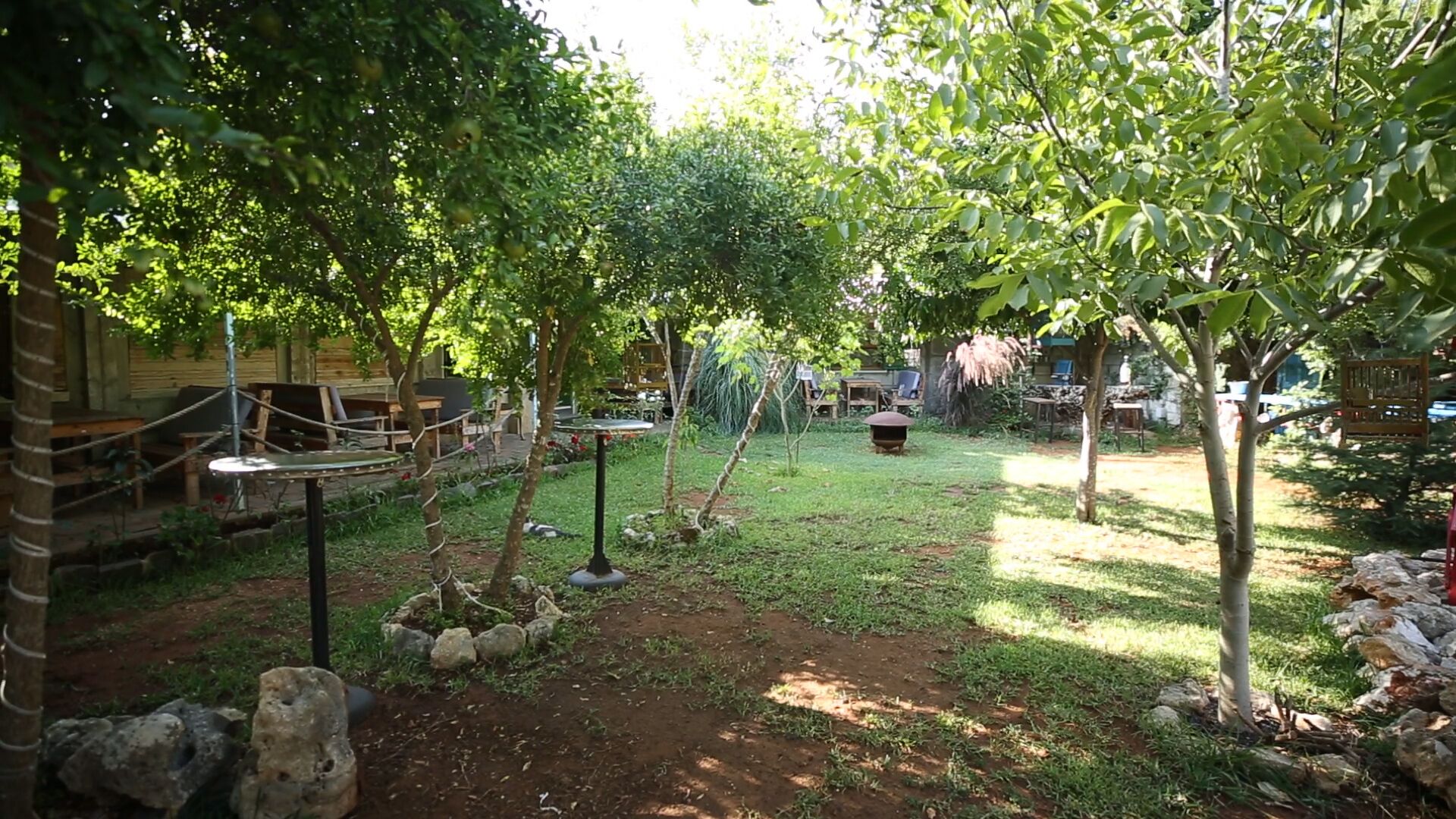 A garden area with tables and chairs, surrounded by trees and a small pond.