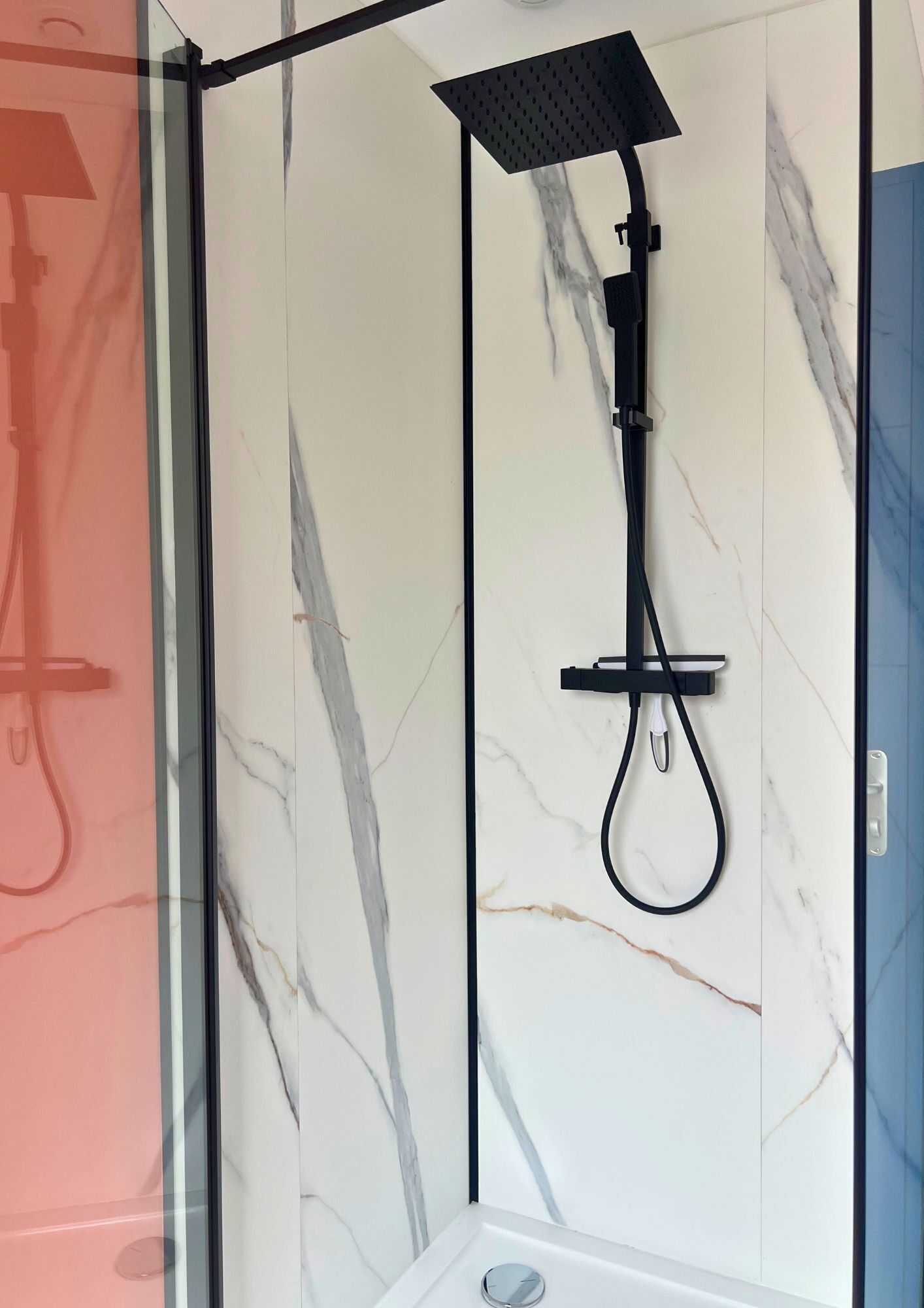A shower enclosure with a black showerhead and hose, set against a marble wall.