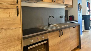 A modern kitchen with wooden cabinets, a stainless steel range hood, a black faucet, and a built-in oven. - Apart'Moment EN GROUPE - L'Horizon Bleu (Bourbourg)