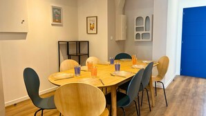 A dining area with a wooden table set for six, surrounded by six chairs, and a blue door in the background. - Apart'Moment EN GROUPE - L'Horizon Bleu (Bourbourg)