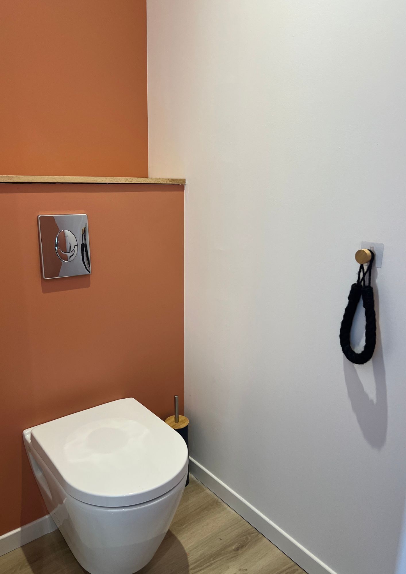 A small, modern bathroom with a white toilet, a wooden floor, and an orange wall.
