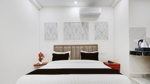 A modern hotel room with a large bed, a nightstand, a bedside table with a phone, and a wall-mounted air conditioner.