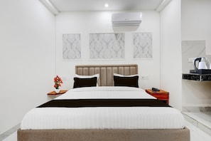 Une chambre d’hôtel moderne avec un grand lit, une table de chevet, une petite table de nuit avec un téléphone et un climatiseur fixé au mur.