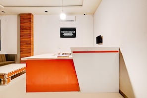 Un espace d’accueil avec un bureau blanc, un mur d’accent rouge, un panneau en bois et un panneau indiquant que l’établissement est géré par une entreprise.