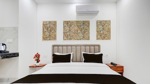 A hotel room with a bed, a nightstand, a wall-mounted air conditioner, and three abstract paintings.