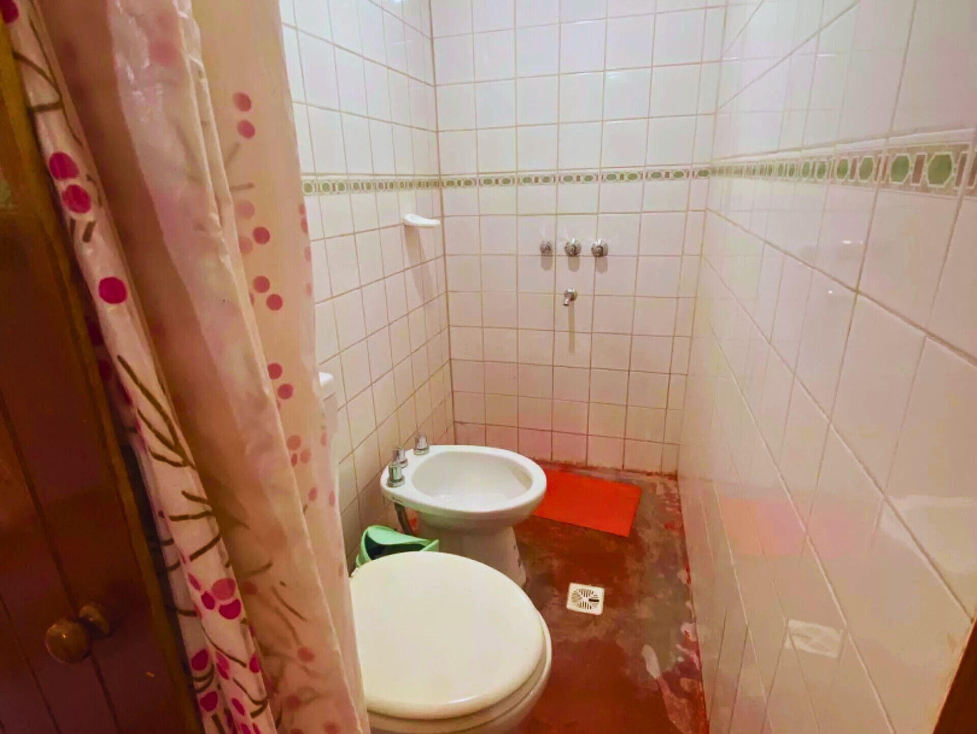 Une petite salle de bain aux murs recouverts de carreaux blancs, avec des toilettes, un bidet et un espace douche.