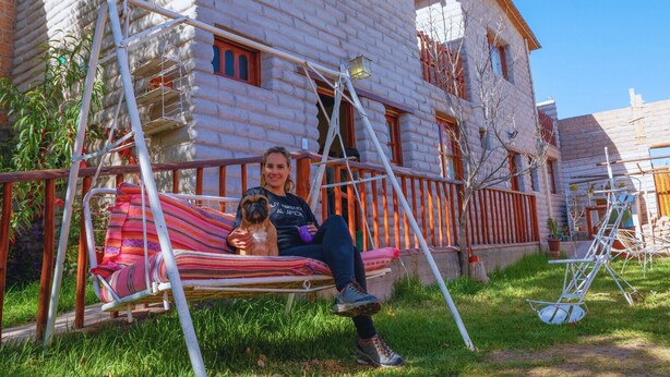 Une personne est assise dans un hamac devant un bâtiment en pierre, protégé par une clôture en bois.
