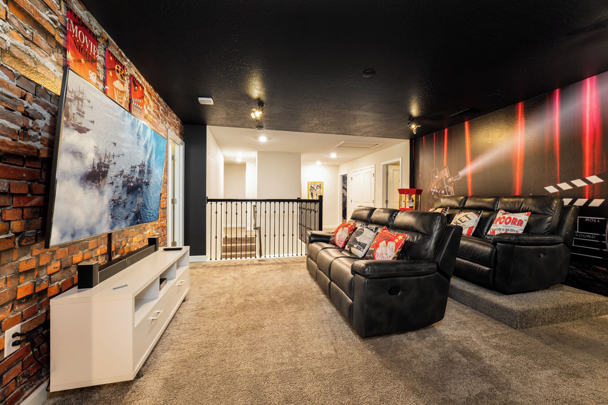 Sala de cine en casa con pared de ladrillo, un televisor de pantalla plana grande, mueble blanco de entretenimiento y sillones de cuero negro.
